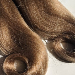 May include: Two strands of brown synthetic hair with a slight shimmer. The hair is curled at the ends.