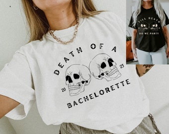 May include: White t-shirt with a black graphic of two skulls and the text "Death of a Bachelorette" with the numbers 20 and 23.