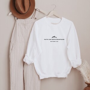 May include: White long-sleeve sweatshirt with the text "Faith can move mountains" and "Matthew 17:20" printed on the front.