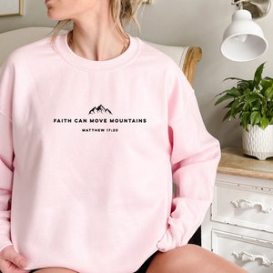 May include: Pink sweatshirt with the text "Faith can move mountains" and "Matthew 17:20" in black.