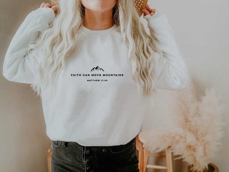 May include: White long-sleeve sweatshirt with black text that reads "Faith Can Move Mountains Matthew 17:20".