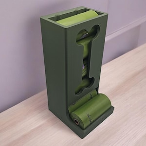 May include: A green plastic dog waste bag dispenser with a bone-shaped cutout. The dispenser holds three rolls of green dog waste bags.