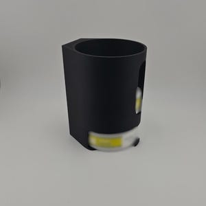 May include: A black, geometric-shaped cup holder with a cylindrical interior and a rectangular base. The holder has a cutout on the side and is designed to hold a small, cylindrical object. The object appears to be a light.