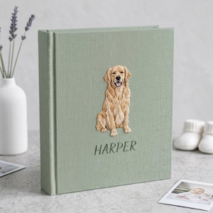 May include: A sage green fabric-covered photo album featuring an embroidered golden retriever sitting in the center. Below the dog, the name HARPER is embroidered in a matching green thread. The album has a textured linen-like finish.