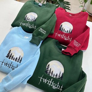 May include: Four crewneck sweatshirts in shades of green, red, and blue. Each sweatshirt features an embroidered design of a full moon, trees, and the word "twilight." Some sleeves have additional text: "Matron of honor," "Where the hell have you been loca," and "Bride."