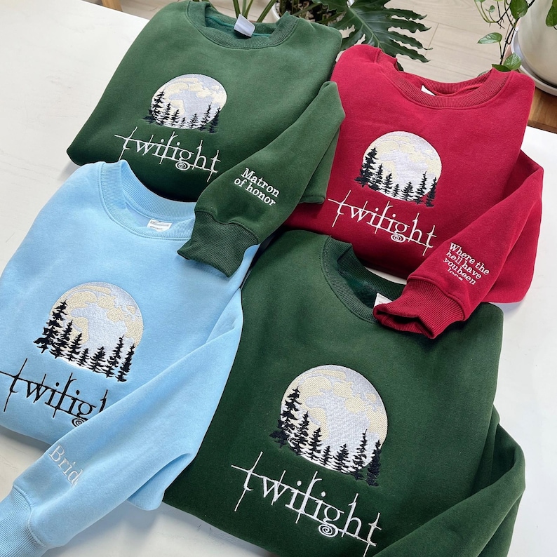 May include: Four crewneck sweatshirts in shades of green, red, and blue. Each sweatshirt features an embroidered design of a full moon, trees, and the word "twilight." Some sleeves have additional text: "Matron of honor," "Where the hell have you been loca," and "Bride."