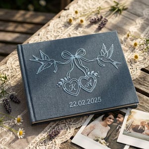May include: A rectangular photo album with a blue herringbone fabric cover featuring white embroidered details. The design includes two birds holding a ribbon tied to two heart-shaped frames containing the letters K and A, with 22.02.2025 below.