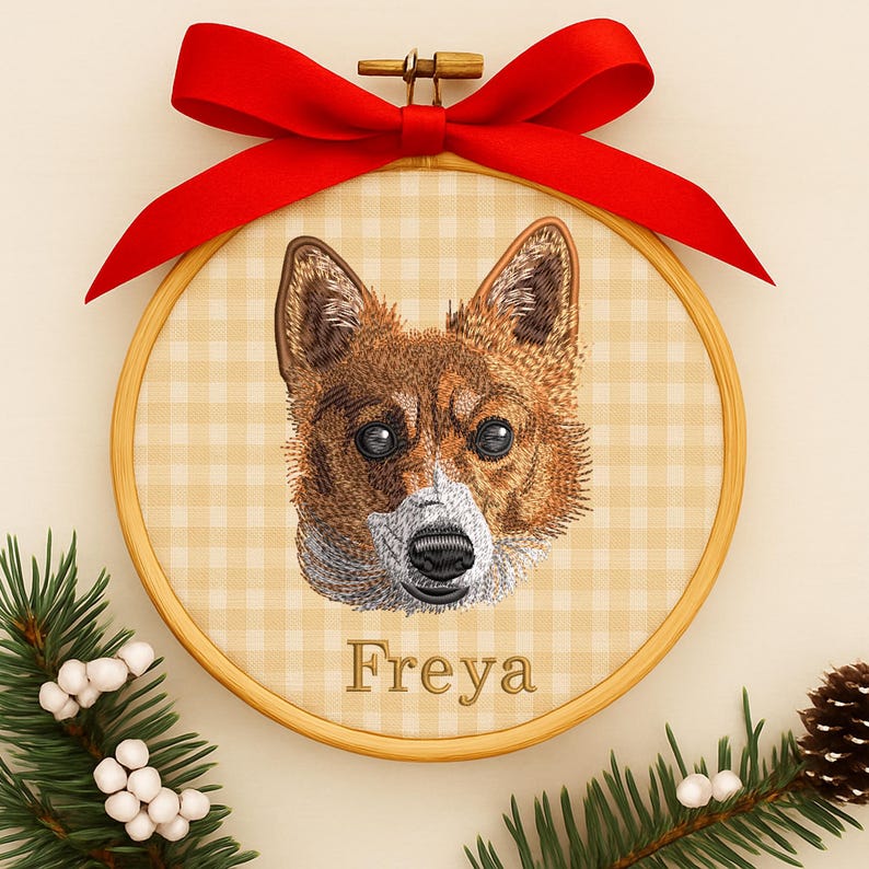 May include: Embroidered dog portrait in a wooden hoop, featuring a brown and white dog with the name "Freya" below. The hoop is adorned with a red ribbon bow at the top and surrounded by greenery and berries.