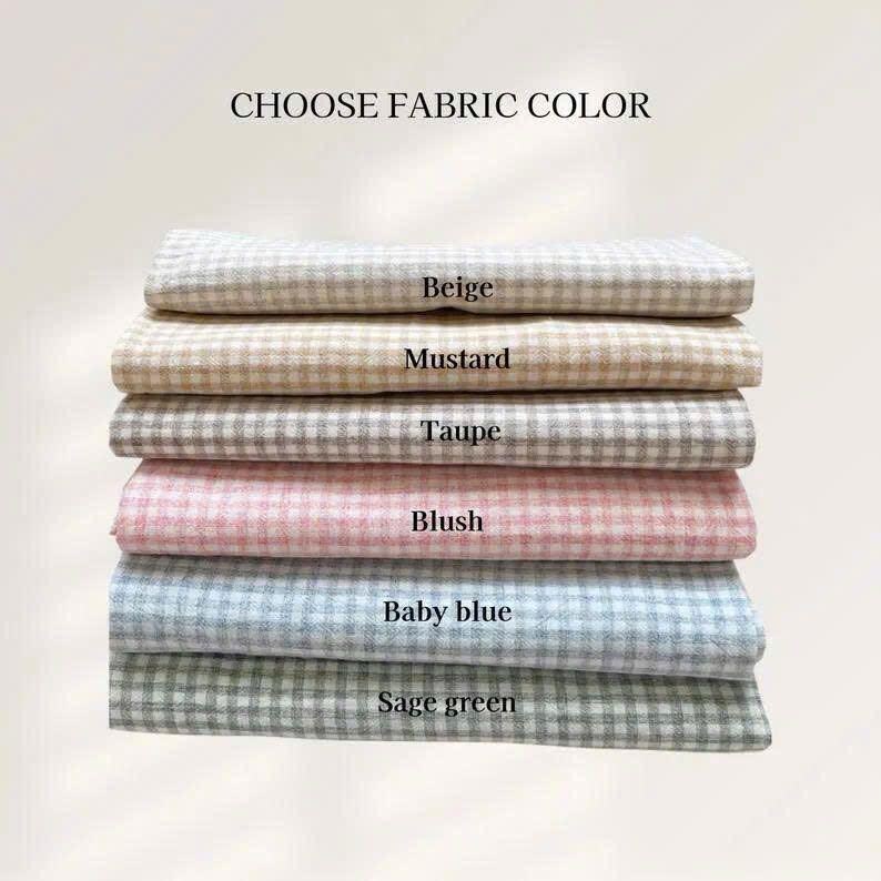 May include: A stack of fabric samples in various colors, including beige, mustard, taupe, blush, baby blue, and sage green. Each fabric has a checkered pattern. The text "CHOOSE FABRIC COLOR" is at the top.