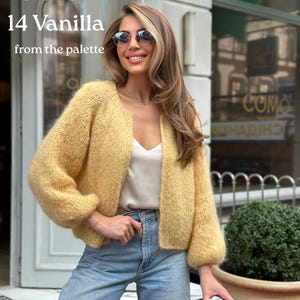 May include: A soft, chunky knit cardigan in a pale yellow vanilla colour with long sleeves and an open front. The garment is worn over a simple cream-coloured camisole and light blue denim jeans. Text on the image reads Color 14 Vanilla from the palette.