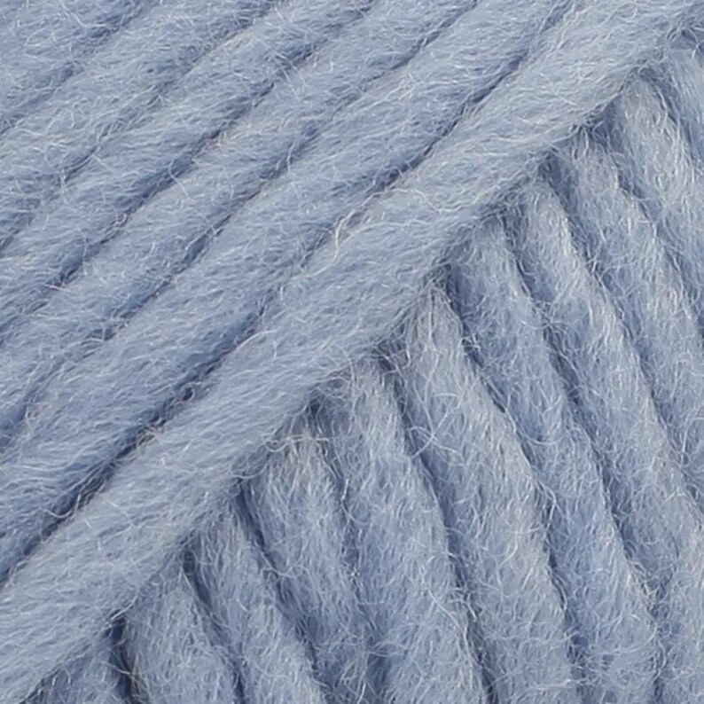 May include: A close-up view of light blue yarn featuring a thick, multi-ply twisted construction with a soft, fuzzy texture. The individual strands are tightly wound together, creating a consistent diagonal pattern across the entire surface.