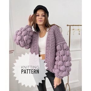 Puede incluir: Un patrón de tejido para un cárdigan morado con mangas grandes y abullonadas. El cárdigan tiene un frente simple y abierto y está hecho con un hilo grueso.