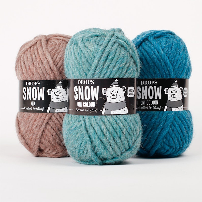 May include: Three skeins of thick yarn in dusty pink, light teal, and dark blue. Each skein features a black paper label with the text DROPS SNOW, a graphic of a bear wearing a hat and scarf, and the phrase Excellent for felting.