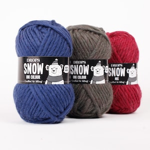 May include: Three balls of thick yarn in blue, dark grey, and red. Each ball has a black paper label featuring the text DROPS SNOW, a graphic of a bear wearing a hat and scarf, and the words 100% WOOL and Excellent for felting.