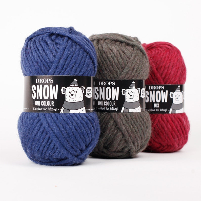 May include: Three balls of thick yarn in blue, dark grey, and red. Each ball has a black paper label featuring the text DROPS SNOW, a graphic of a bear wearing a hat and scarf, and the words 100% WOOL and Excellent for felting.