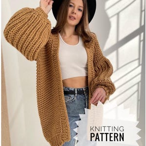 May include: A chunky knit cardigan in a warm camel colour featuring oversized balloon sleeves and a ribbed texture. The garment is worn over a white crop top and blue denim jeans. A black hat is worn on the head. Text reads KNITTING PATTERN.