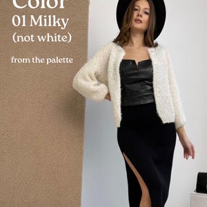 May include: A milky-coloured, open-front knit cardigan with long sleeves, worn over a black leather-look corset top and a black ribbed midi skirt with a side slit. A black wide-brimmed hat is worn. Text reads: Color 01 Milky (not white) from the palette.