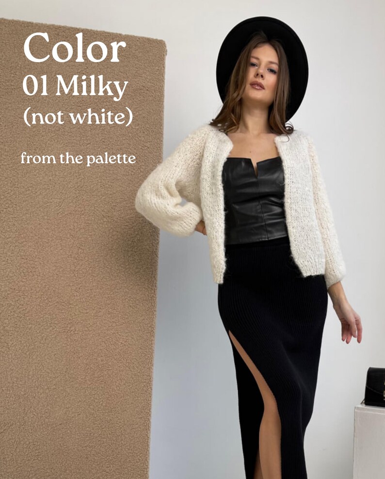May include: A milky-coloured, open-front knit cardigan with long sleeves, worn over a black leather-look corset top and a black ribbed midi skirt with a side slit. A black wide-brimmed hat is worn. Text reads: Color 01 Milky (not white) from the palette.