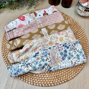May include: Five colourful fabric headbands with floral and geometric patterns. Each headband has a label that says "Happy & La Chouquette" in white text.