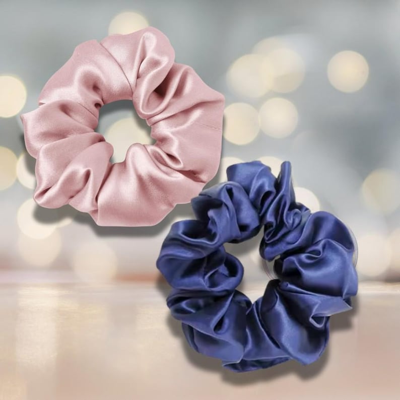 May include: Two satin scrunchies. One is a soft pink, the other is a deep blue. The fabric is gathered and ruched, creating a voluminous, textured appearance. These hair accessories are designed to hold hair in place.
