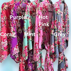 May include: A display of floral print robes in coral, purple, mint, hot pink, and grey. Each robe is hanging on a black hanger. The robes are labeled with their respective colors.