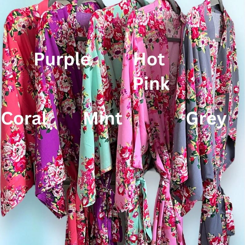 May include: A display of floral print robes in coral, purple, mint, hot pink, and grey. Each robe is hanging on a black hanger. The robes are labeled with their respective colors.