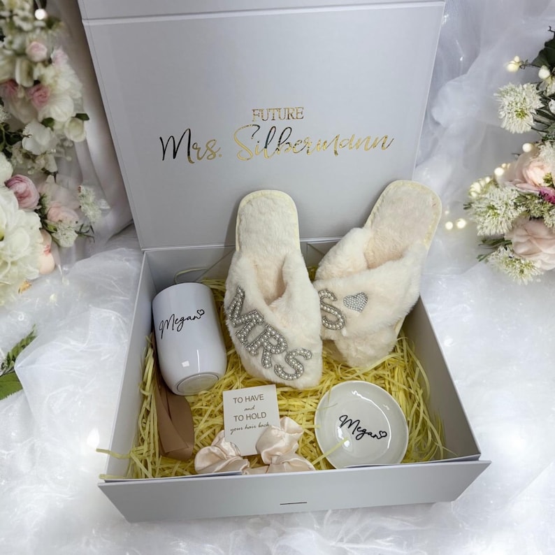 May include: A white gift box containing a white mug, two pairs of white slippers with rhinestones, a small white dish, and two white hair scrunchies. The box is decorated with the text "Future Mrs. Silbermann".