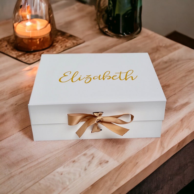 May include: White gift box with a gold ribbon and the name "Elizabeth" printed on the top.