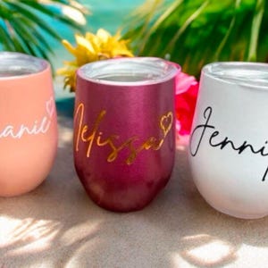 May include: Three personalised stainless steel wine tumblers with the names Stephanie, Melissa, and Jennifer. The tumblers are in pink, burgundy, and white.