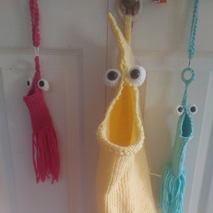 May include: Three crocheted hanging toy bags with googly eyes. The bags are yellow, blue, and pink with fringe at the bottom.