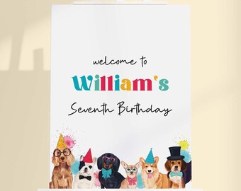 May include: A white rectangular sign on an easel featuring the text "welcome to William's Seventh Birthday" in black and colorful lettering. Below the text are five illustrated dogs wearing party hats, bow ties, and glasses with colorful accents.