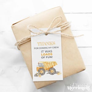 Può includere: Un regalo confezionato con un'etichetta che recita "GRAZIE PER ESSERTI UNITO AL MIO TEAM, È STATO UN DIVERTIMENTO!" L'etichetta presenta un'illustrazione di un dumper giallo. Il regalo è avvolto in carta marrone e legato con spago.