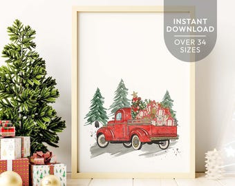May include: A framed watercolor print featuring a red vintage pickup truck carrying a decorated Christmas tree and wrapped gifts in its bed, set against a backdrop of green pine trees. The artwork is displayed in a light wood frame.