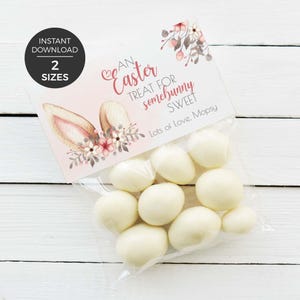 May include: A transparent bag containing white, egg-shaped sweets. The bag is sealed with a card decorated with bunny ears, flowers, and the words "An Easter Treat for somebunny Sweet."