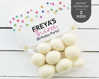 May include: A clear plastic treat bag filled with white round candies, topped with a white paper header featuring colorful confetti dots, gold starburst accents, and the black and pink text "FREYA'S third Birthday Party!" printed on the front.