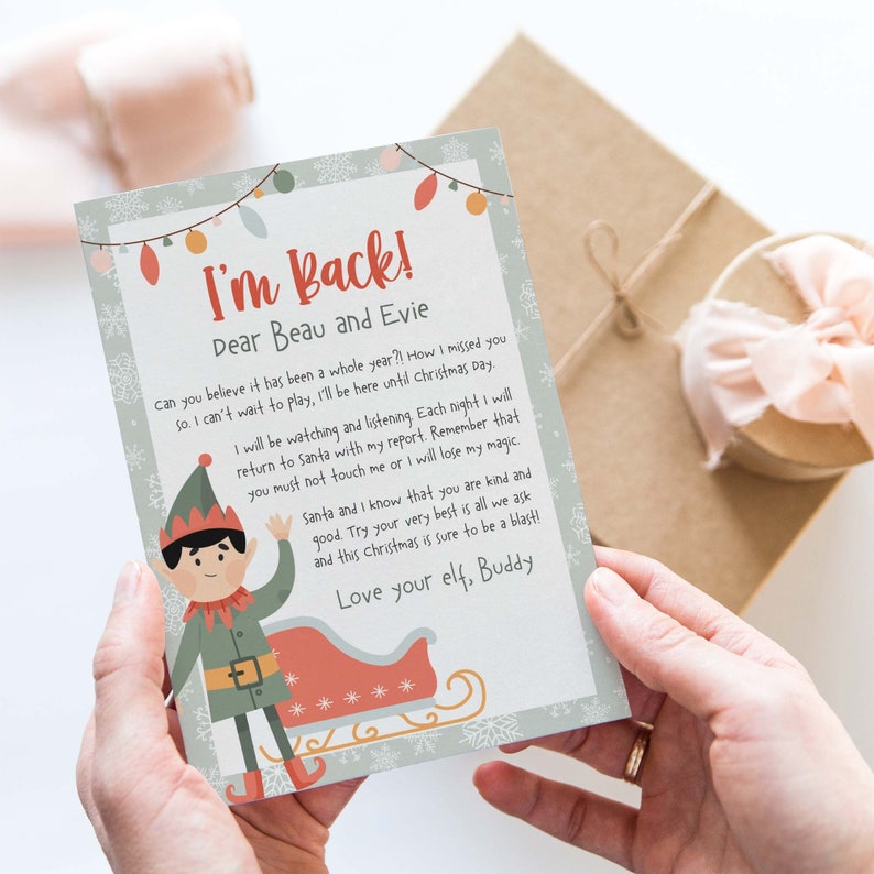 May include: A green elf with a red hat and a white beard is holding a sign that says "I'm Back! Dear Beau and Evie". The sign is decorated with snowflakes and a string of lights. The elf is standing in front of a red sleigh with white stars.