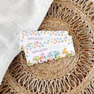 Può includere: Due incarti rettangolari per barrette di cioccolato con un motivo di uova di Pasqua colorate e quattro gnomi con orecchie da coniglio. Il testo recita Happy Easter! Lots of love, the Cottontail family in caratteri viola e verde chiaro.