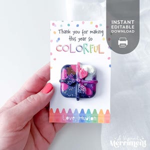 Può includere: Un pastello a cera multicolore a forma di pacchetto regalo con fiocco, fissato su un cartoncino bianco con coriandoli colorati, il testo "Thank you for making this year so COLORFUL" e il nome "Love, Hudson" in basso.