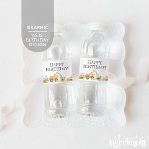 Könnte beinhalten: Zwei transparente Plastikwasserflaschen mit weißen Etiketten mit der Aufschrift "HAPPY BIRTHDAY!" und Illustrationen von Baumaschinen. Die Flaschen stehen auf einem weißen, dekorativen Teller, mit dem Text "GRAPHIC 'AS IS' BIRTHDAY DESIGN" im Hintergrund.