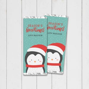 May include: Two candy bar wrappers with a teal background and a repeating snowflake pattern. Each wrapper features a cartoon penguin wearing a red hat and scarf. The text "SEASON'S Greetings!" and "LOVE MADISON" are printed on the wrappers.