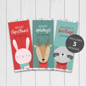 Könnte beinhalten: Drei festliche Schokoladenriegel-Verpackungen mit Weihnachtsgrüßen. Designs umfassen ein Kaninchen, ein Rentier und einen Waschbären, die jeweils einen Pullover tragen. Die Verpackungen zeigen die Sätze "Merry Christmas!", "Happy Holidays!" und "Season's Greetings!"