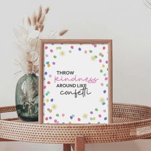 Könnte beinhalten: Gerahmter Druck mit dem Text "Throw kindness around like confetti", umgeben von bunten Konfetti-Punkten. Der Rahmen ist hellbraun. Auf einem gewebten Tablett platziert.