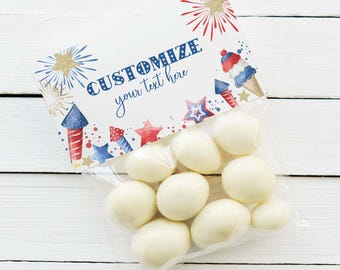 Puede incluir: Una bolsa de plástico transparente llena de dulces redondos blancos, con una etiqueta de papel rectangular con ilustraciones de fuegos artificiales, estrellas y helados en rojo, blanco y azul con el texto CUSTOMIZE your text here.