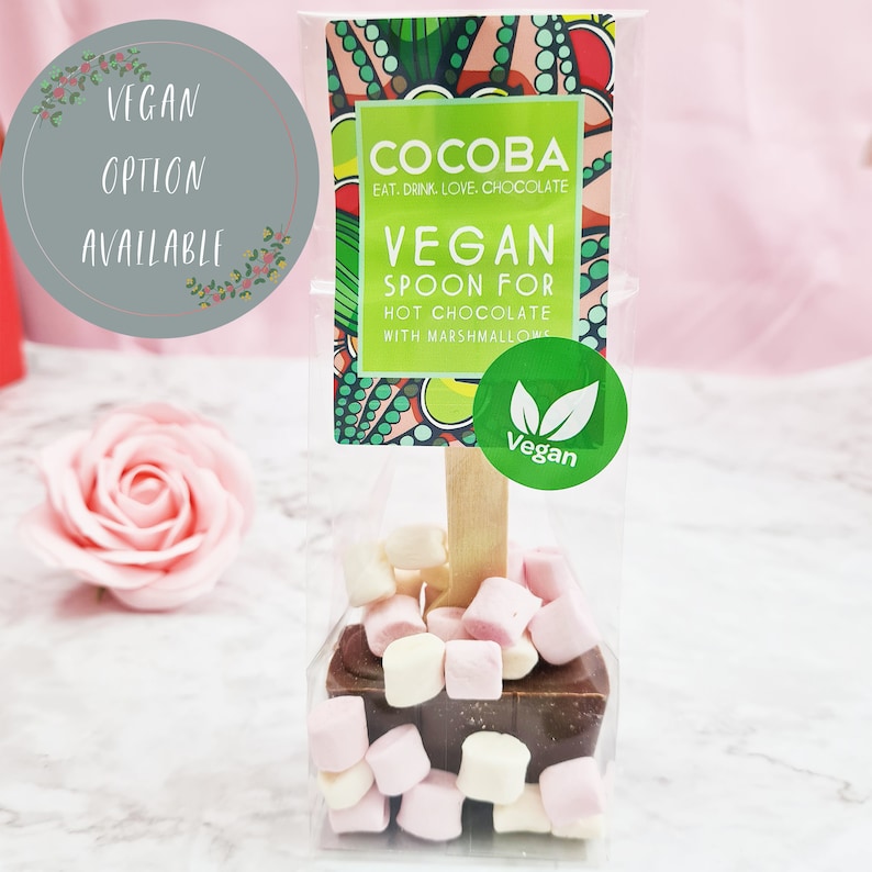 K&ouml;nnte beinhalten: Ein veganer Hei&szlig;schokoladenl&ouml;ffel mit Marshmallows. Der L&ouml;ffel besteht aus Schokolade und ist mit Mini-Marshmallows belegt. Die Verpackung ist aus durchsichtigem Plastik und tr&auml;gt ein Etikett mit der Aufschrift "Cocoba Eat. Drink. Love. Chocolate Vegan Spoon for Hot Chocolate with Marshmallows".