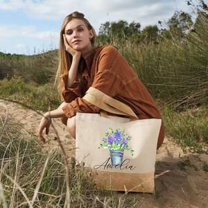 May include: A personalized tote bag with a floral design and the name "Amelia" printed on the front. The bag is made of natural canvas and has a jute trim.