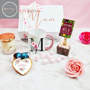 K&ouml;nnte beinhalten: Eine Geschenkbox f&uuml;r eine Mutter mit einer Tasse, einer Kerze, einer herzf&ouml;rmigen Schachtel Pralinen, einem hei&szlig;en Schokoladenl&ouml;ffel und einer rosa Rose. Die Tasse hat ein Blumenmuster und die Worte "Mama" darauf. Die Kerze hat einen goldenen Deckel und die Worte "Mama" darauf. Die herzf&ouml;rmige Schachtel Pralinen hat ein Blumenmuster und die Worte "Mama" darauf. Der hei&szlig;e Schokoladenl&ouml;ffel hat eine Marshmallow darauf. Die rosa Rose ist eine einzelne Rose.