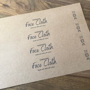 以下が含まれることがあります： 4枚の茶色の紙ラベルに「HANDMADE Face Cloth Made with 100% soft cotton」というテキストが印刷されています。ラベルには、右側に洗濯表示も印刷されています。