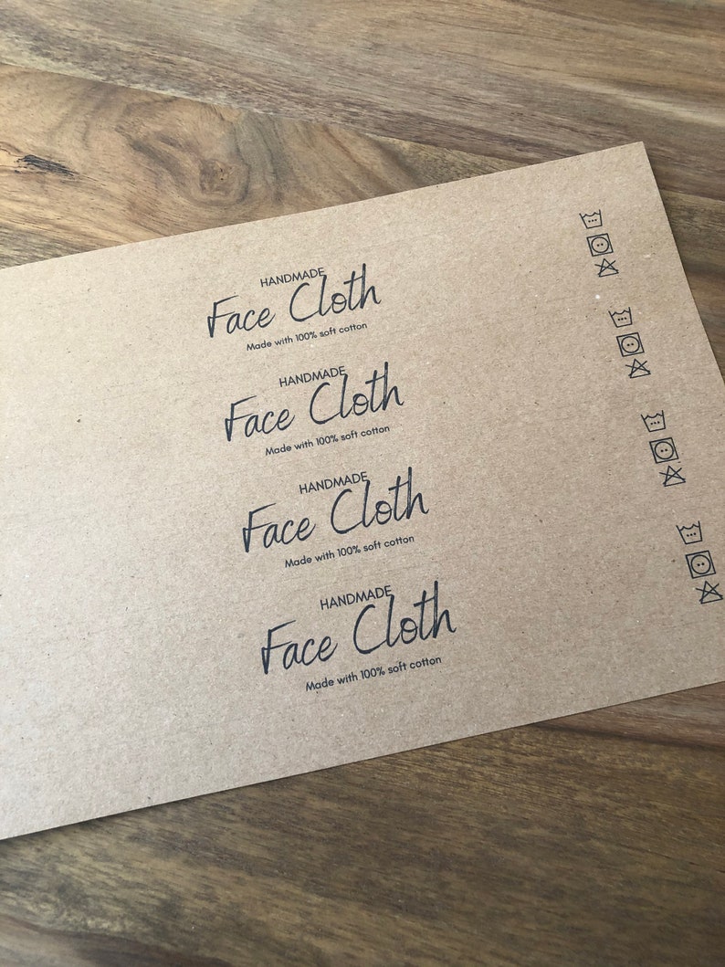 以下が含まれることがあります： 4枚の茶色の紙ラベルに「HANDMADE Face Cloth Made with 100% soft cotton」というテキストが印刷されています。ラベルには、右側に洗濯表示も印刷されています。