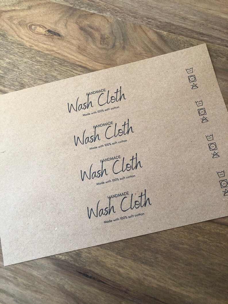 以下が含まれることがあります： 4枚の茶色の紙ラベルに「HANDMADE Wash Cloth Made with 100% soft cotton」というテキストが印刷されています。ラベルには、右側に洗濯表示のシンボルも印刷されています。