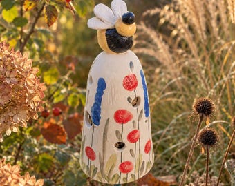 May include: A ceramic bee garden stake featuring a cream-colored conical body decorated with hand-painted red poppies and blue floral stalks. The bee has a yellow and black striped head with white wings and is mounted on a thin green metal rod.